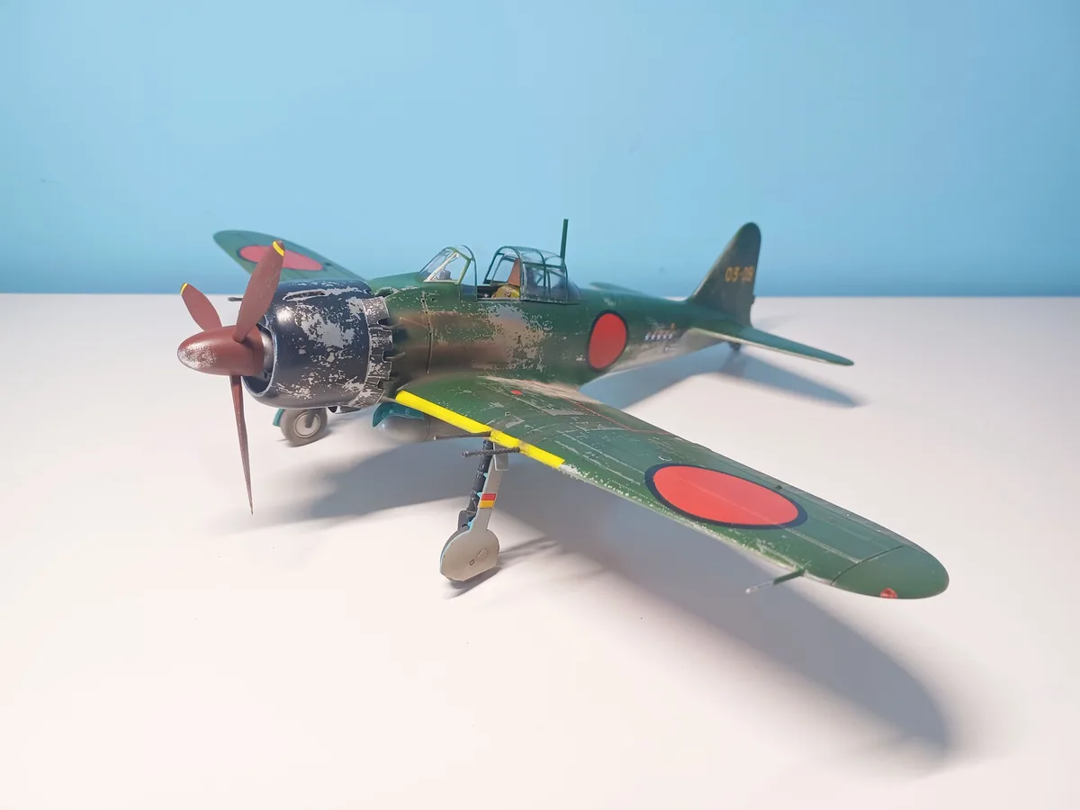A detailed scale model of a green Japanese World War II fighter plane with red circles on the wings and fuselage, shown on a…