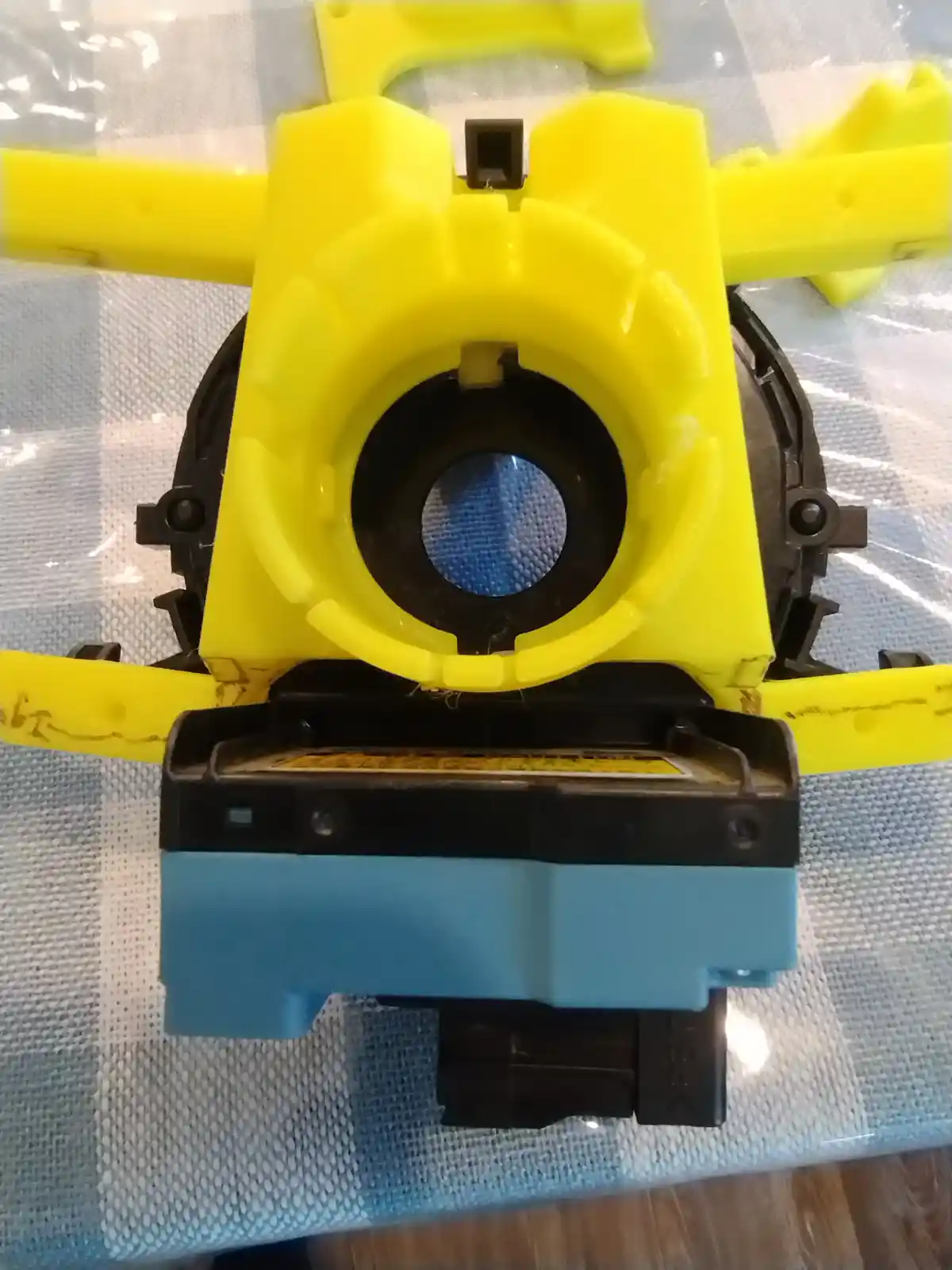 A disassembled yellow and black printer cartridge with its top cover removed, revealing a blue internal component, sits on a…