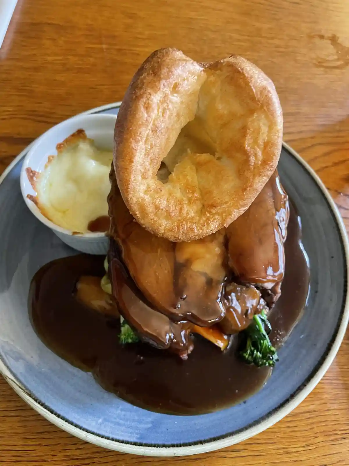 A close-up photo of a traditional British meal featuring a golden-brown Yorkshire pudding perched atop a pile of meat…
