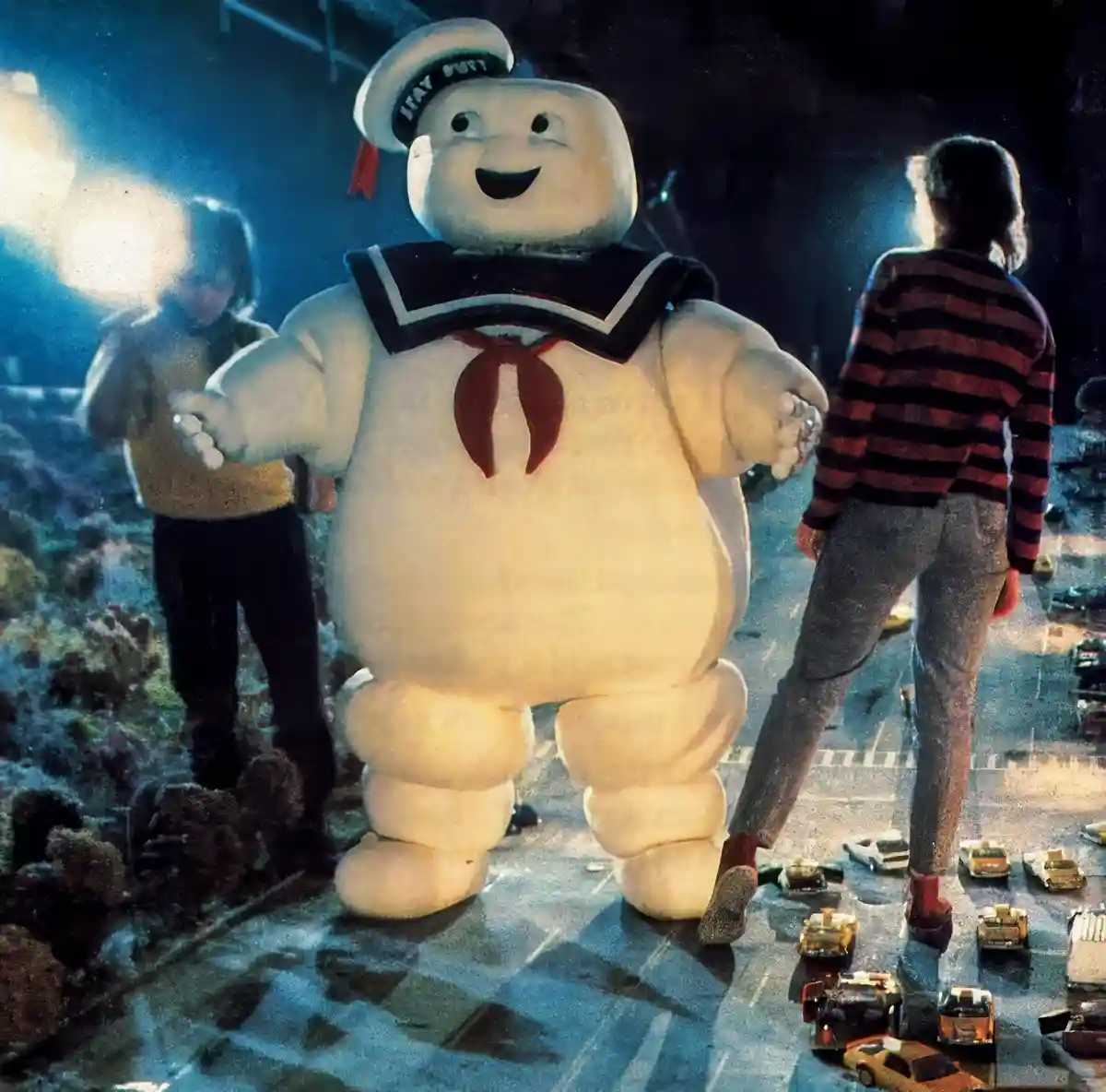 A large, white, marshmallow-like character in a sailor uniform with a red bow and a hat reading 'Stay Puft' stands in a…