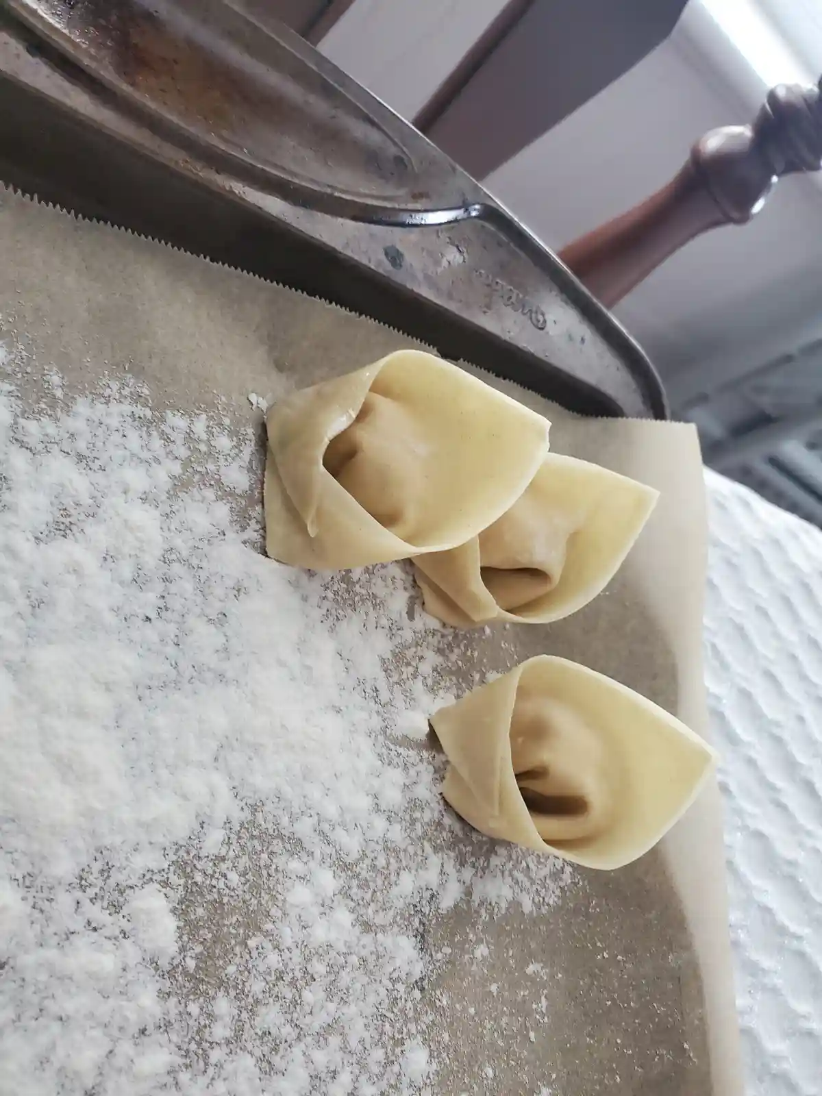 Three handmade dumplings sit on a floured baking sheet, their pleated edges resembling tear-streaked faces. The image is…