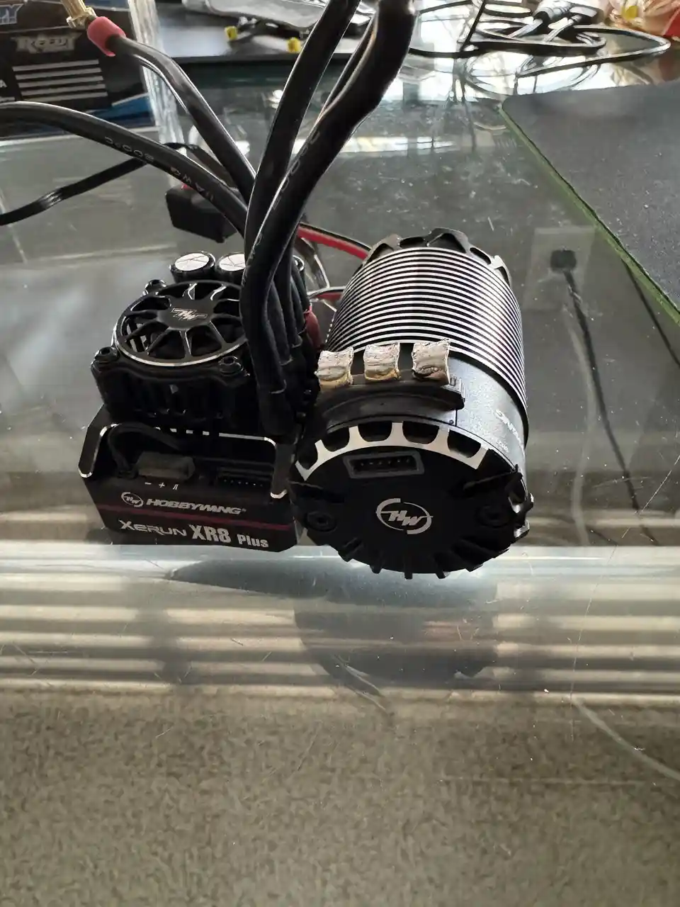 A close-up photo shows a drone motor and electronic speed controller (ESC) combo sitting on a glass table, with numerous…