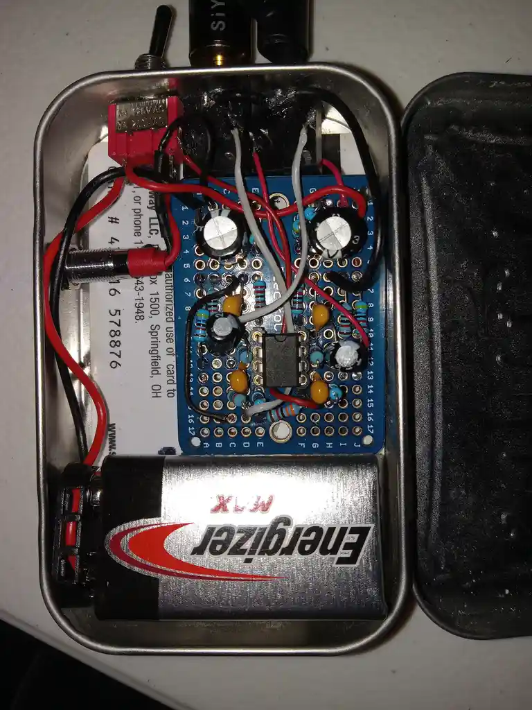 A homemade electronic device built inside a metal tin can, featuring a blue breadboard with various resistors, capacitors…