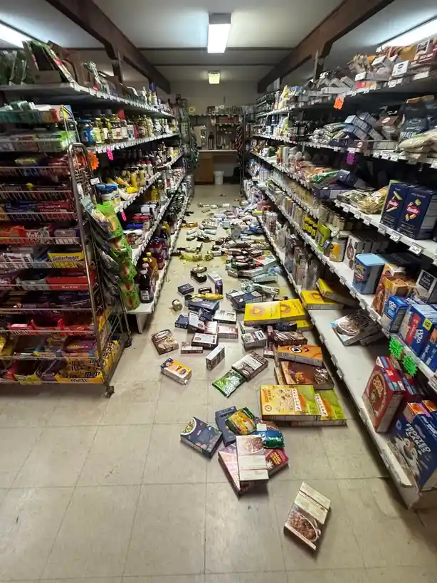 A grocery store aisle is in disarray, with shelves stocked with snacks and canned goods, but the floor is covered in spilled…