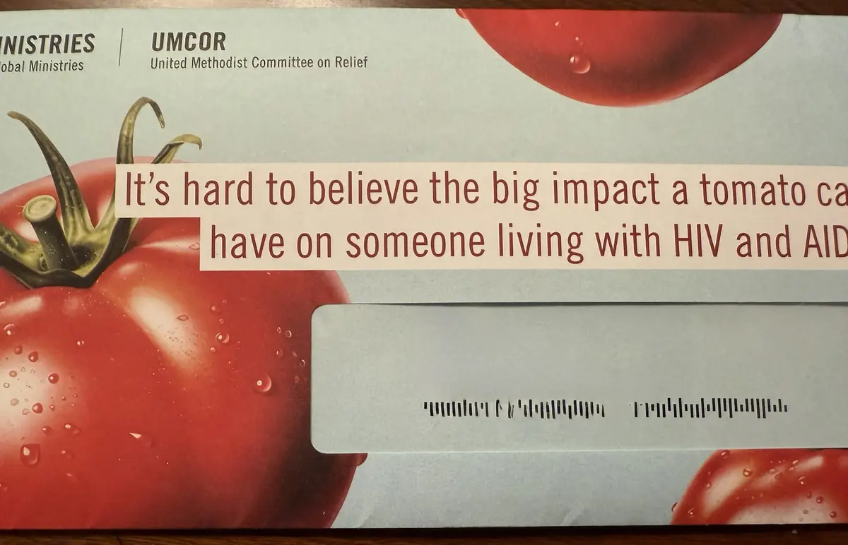 A close-up of a charity donation envelope from UMCOR (United Methodist Committee on Relief) featuring a large, glossy red…