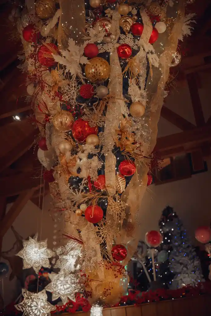 A heavily decorated, vertically oriented Christmas tree is covered in an excessive amount of red and gold ornaments…