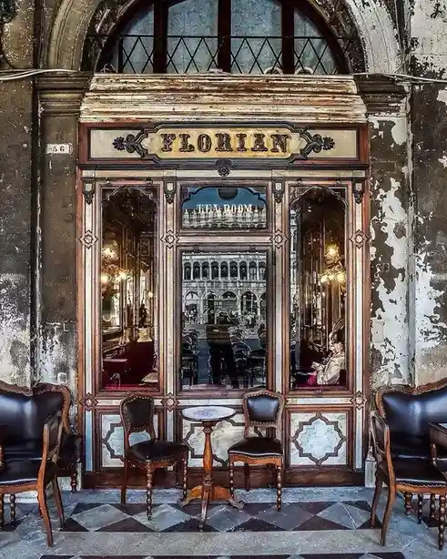 A vintage photograph of the historic Florian tea room in Venice, Italy, showing its ornate wooden facade with the name…
