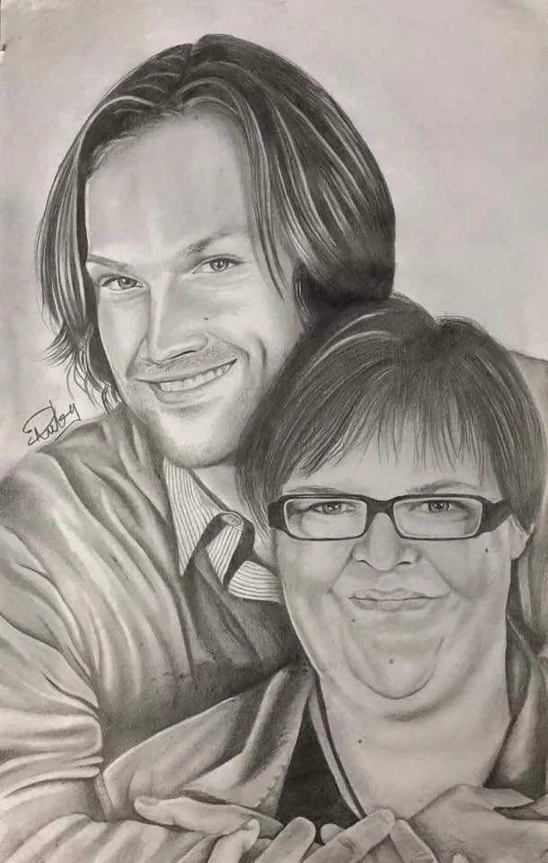 A detailed pencil drawing shows a man with shoulder-length hair smiling behind a woman with glasses and a slight smile. The…