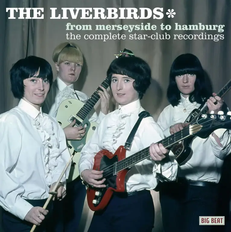 An album cover featuring four women in matching white ruffled shirts and dark pants, holding guitars and drumsticks, posed…