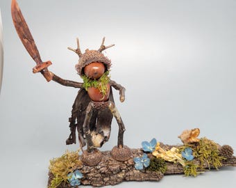 A whimsical, handcrafted figurine depicts a small creature resembling a tree or forest spirit, with a brown acorn-like head…