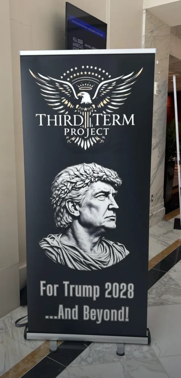 A black banner stand displays a logo with an eagle and stars above the text 'THIRD TERM PROJECT'. Below, a stylized bust of…