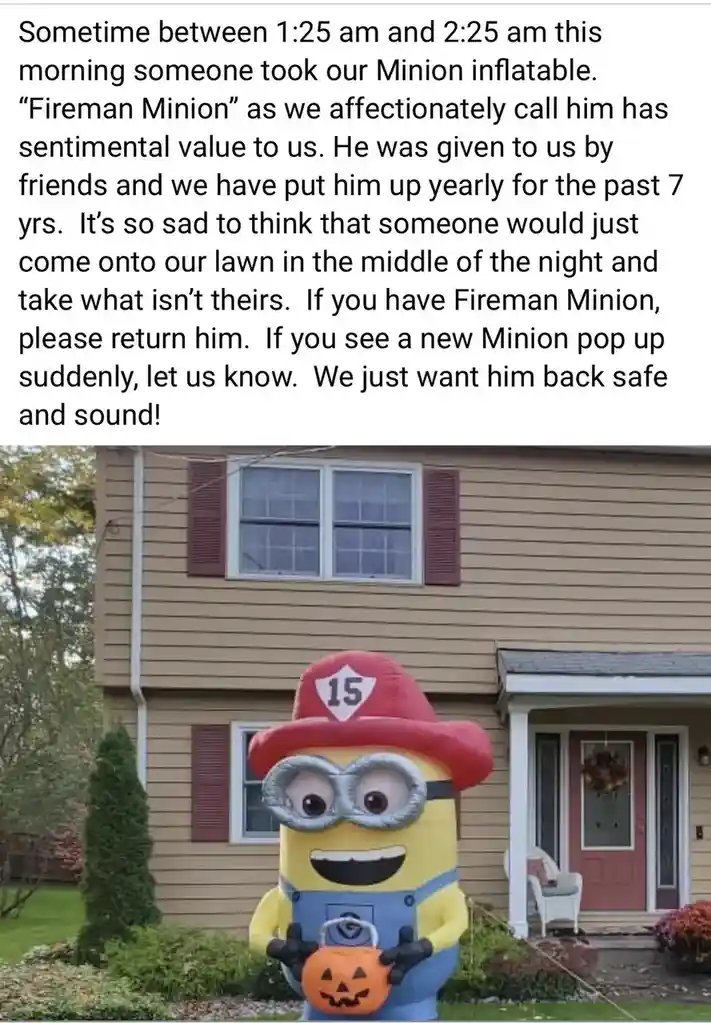 A large inflatable Minion dressed as a firefighter with a red hat marked '15' and holding a pumpkin, stands on a lawn in…