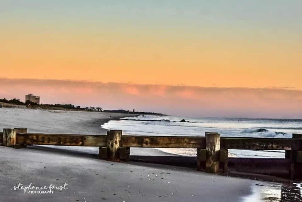 A serene beach sunset photo with a wooden fence in the foreground, gentle waves, and a colorful sky. Overlaid text reads…