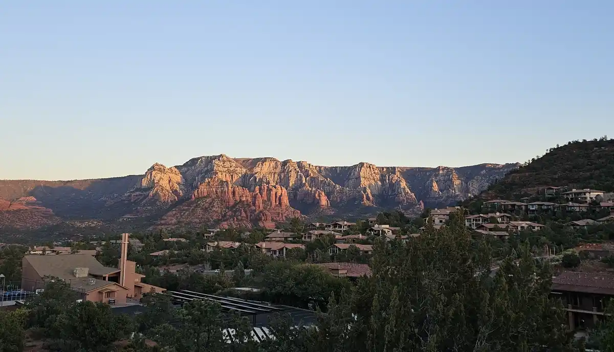 A scenic photo of a residential area nestled against red rock canyon formations at sunset, with houses and trees in the…