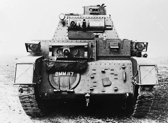 A black and white photograph shows the rear view of a vintage armored tank with riveted metal plating, tracks, and a visible…
