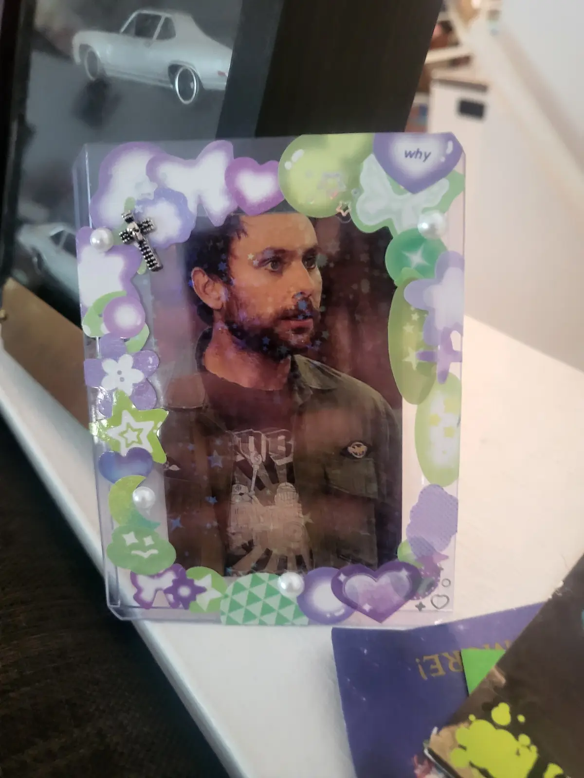 A photo of a man with a surprised or confused expression is framed in a clear plastic holder decorated with purple and green…