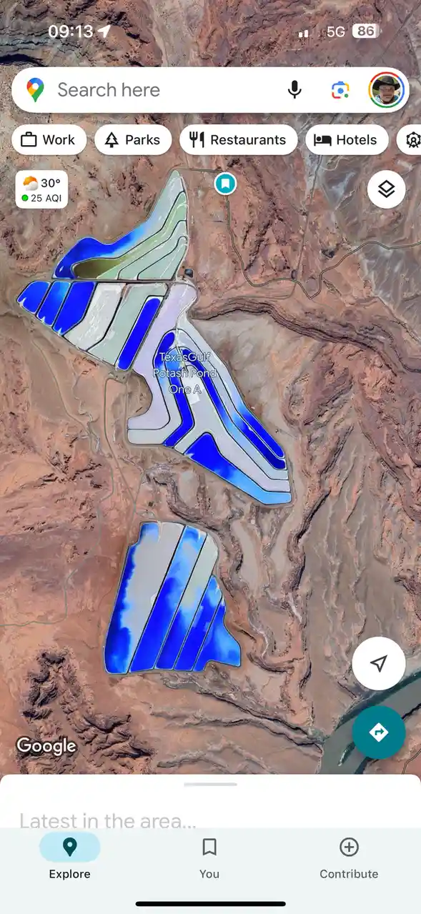 A Google Maps satellite view shows a large, geometrically shaped industrial salt evaporation pond complex in a desert…