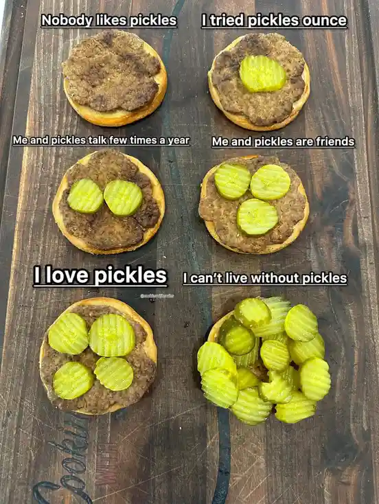 Six burger patties on buns arranged on a wooden cutting board, each progressively covered with more pickle slices…