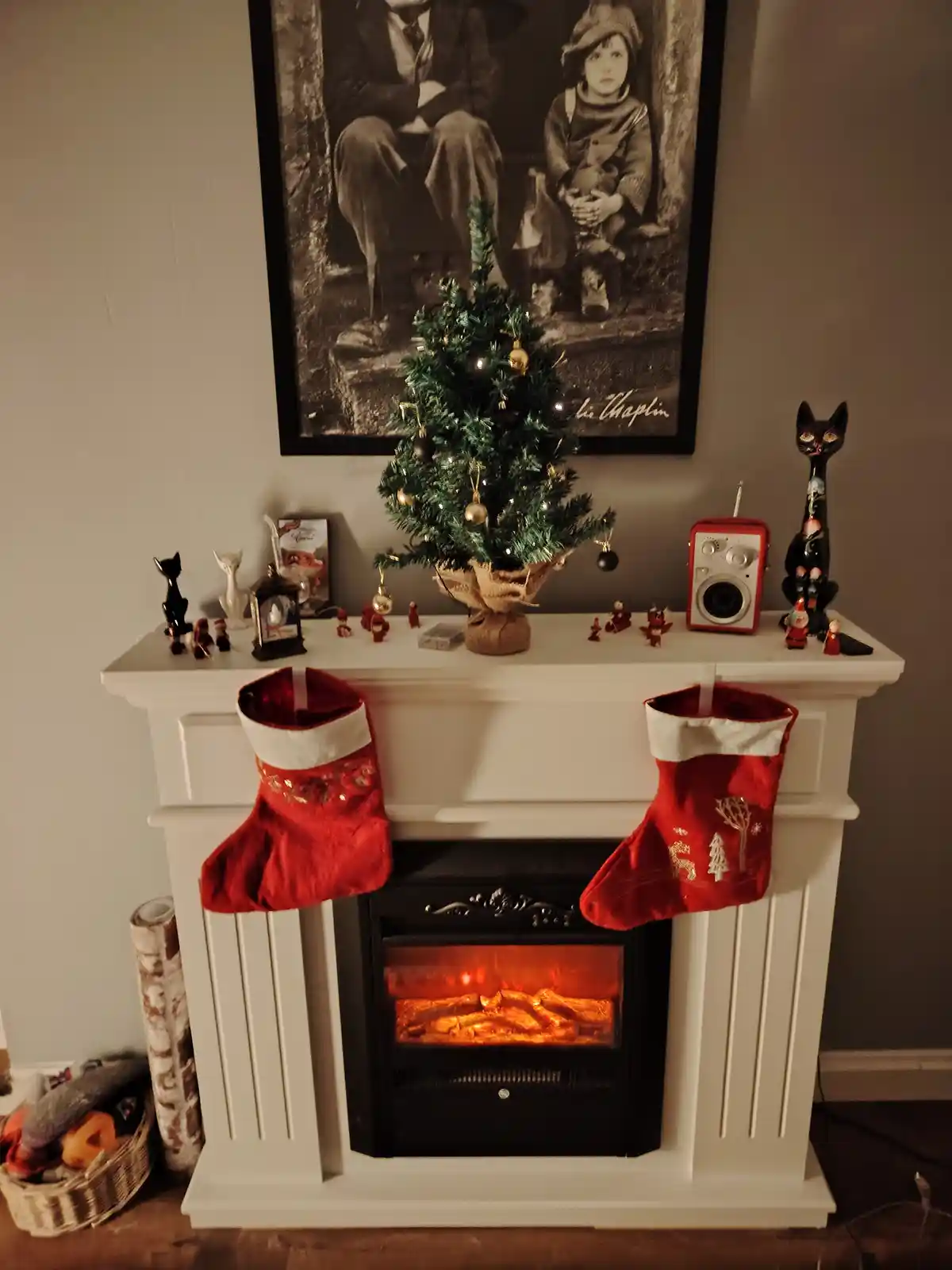 A cozy fireplace with two red stockings hanging on either side, an electric fire glowing inside, and a small decorated…