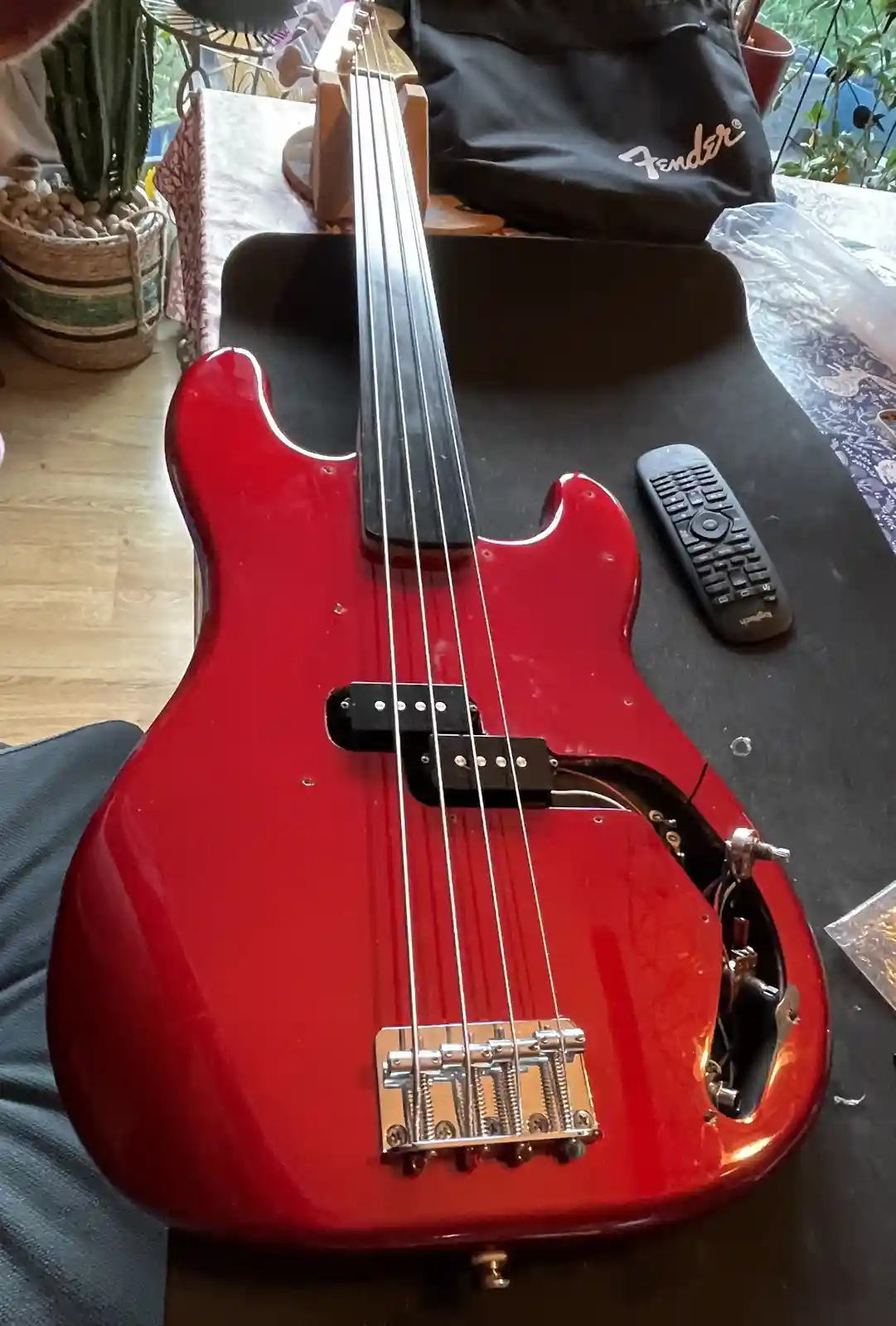 A red electric bass guitar with its body partially disassembled, revealing internal wiring and components, sits on a black…