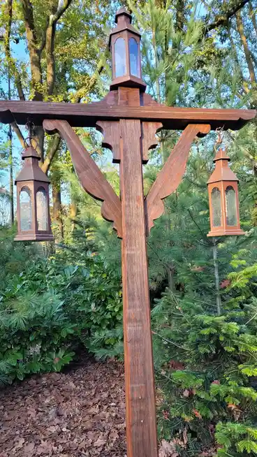 A wooden post with three hanging lanterns, two on sides and one on top, set against greenery and trees. The overlaid text…