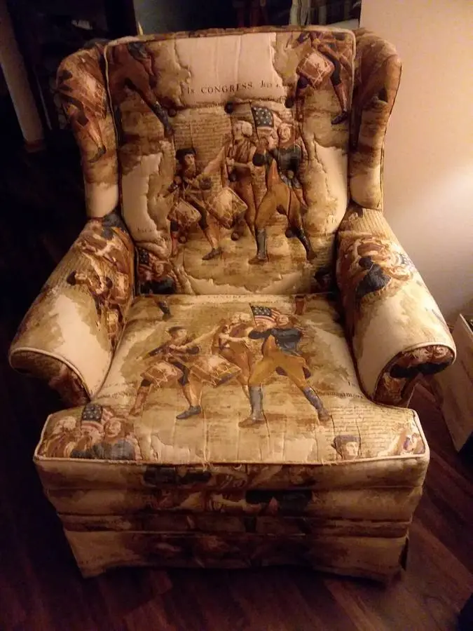 A large, ornate armchair upholstered in fabric depicting historical American Revolutionary War scenes with soldiers and text…