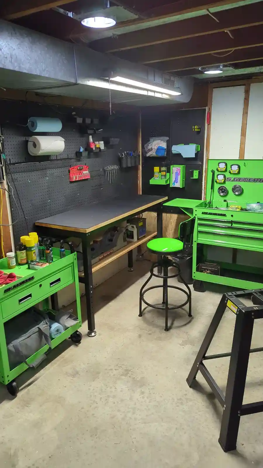 A well-organized garage workshop with black pegboard walls holding tools and supplies, a central workbench, and bright green…