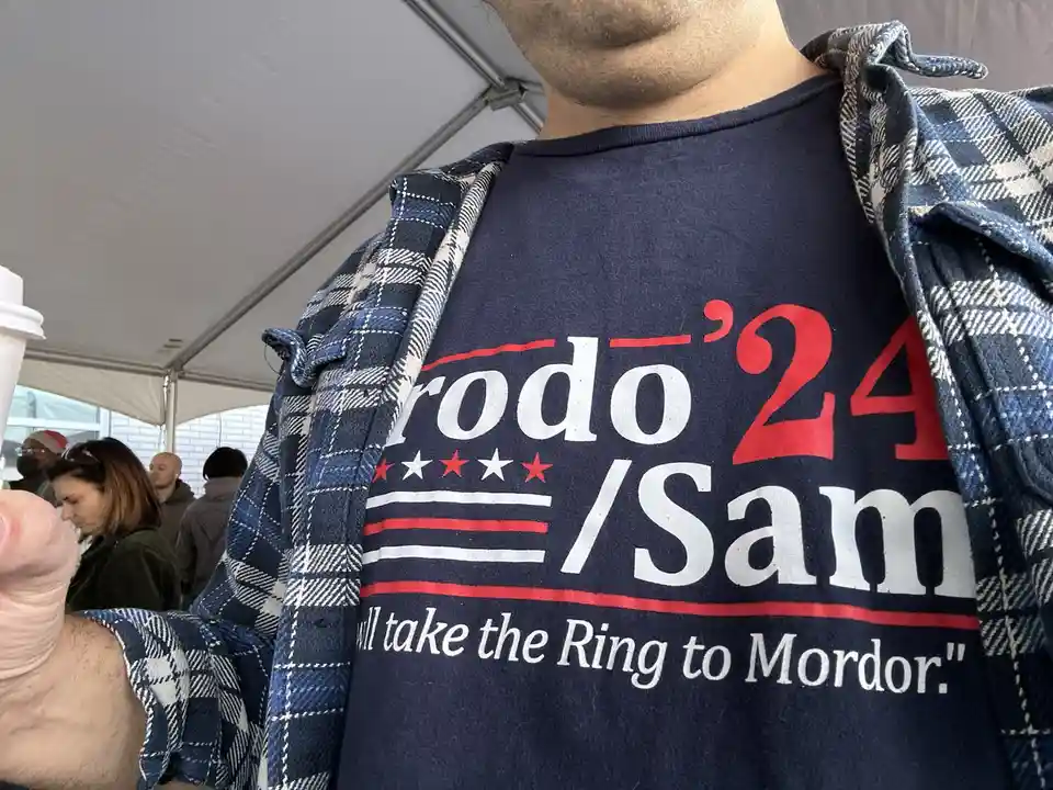 A close-up photo shows a person wearing a dark blue t-shirt with red, white, and blue political-style graphics. The shirt…