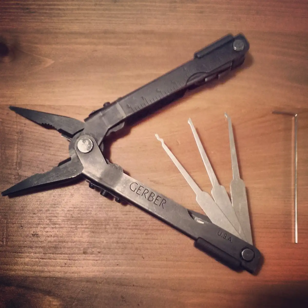 A black Gerber multi-tool is open on a wooden surface, revealing its various tools including pliers, a ruler, and several…