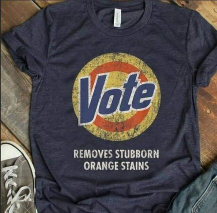 A dark blue t-shirt laid flat on a wooden surface, featuring a circular logo with the word 'Vote' in bold blue letters over…
