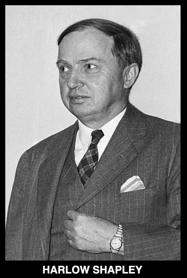 A black-and-white photograph of a man in a pinstripe suit and plaid tie, looking off to the side with a slightly surprised…