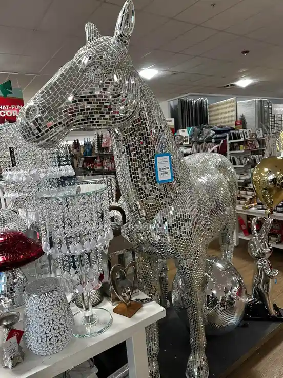 a large, life-sized horse statue covered in reflective silver mirror tiles is displayed in a retail store, with a blue price…