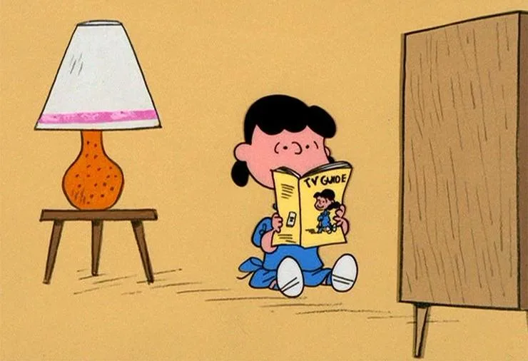 A cartoon girl with black hair sits on the floor in front of a wooden TV cabinet, reading a yellow magazine titled 'TV…