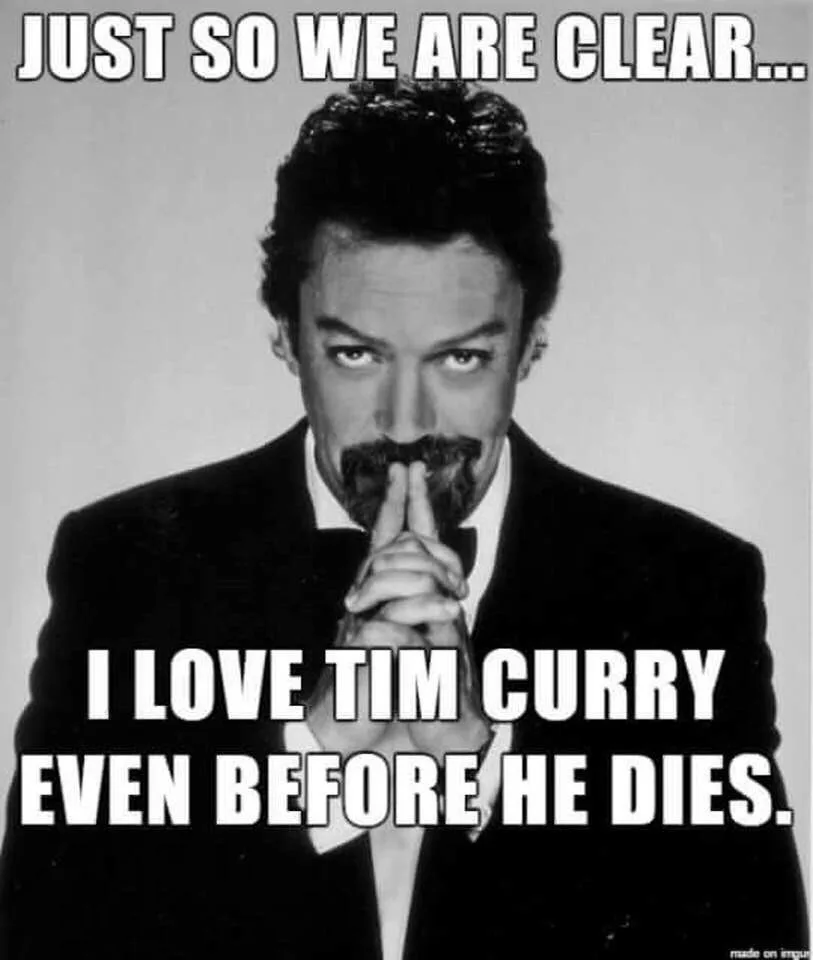 A black-and-white photo of actor Tim Curry, dressed in a suit and bowtie, staring intensely at the viewer with his index…