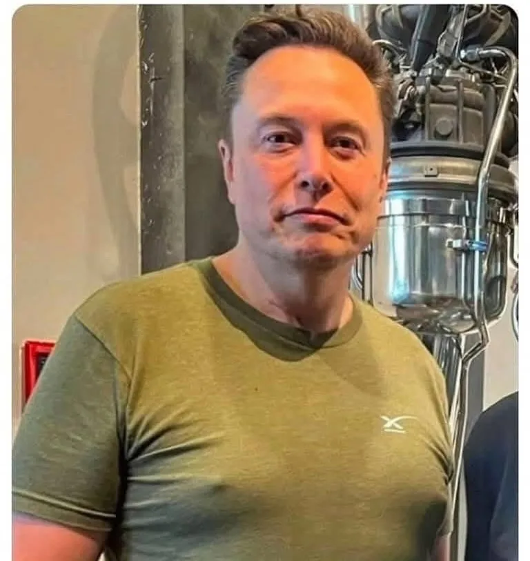 A man with short dark hair and a neutral expression wears a green t-shirt with a small white logo on the left chest. Behind…