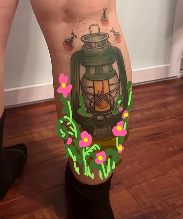 A close-up photo shows a person's lower leg with a detailed tattoo of a green oil lantern containing a flame. The tattoo is…