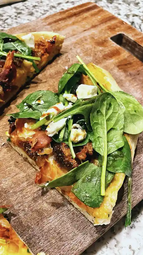 Two slices of gourmet pizza topped with fresh spinach leaves, crumbled white cheese, and drizzled balsamic reduction sit on…
