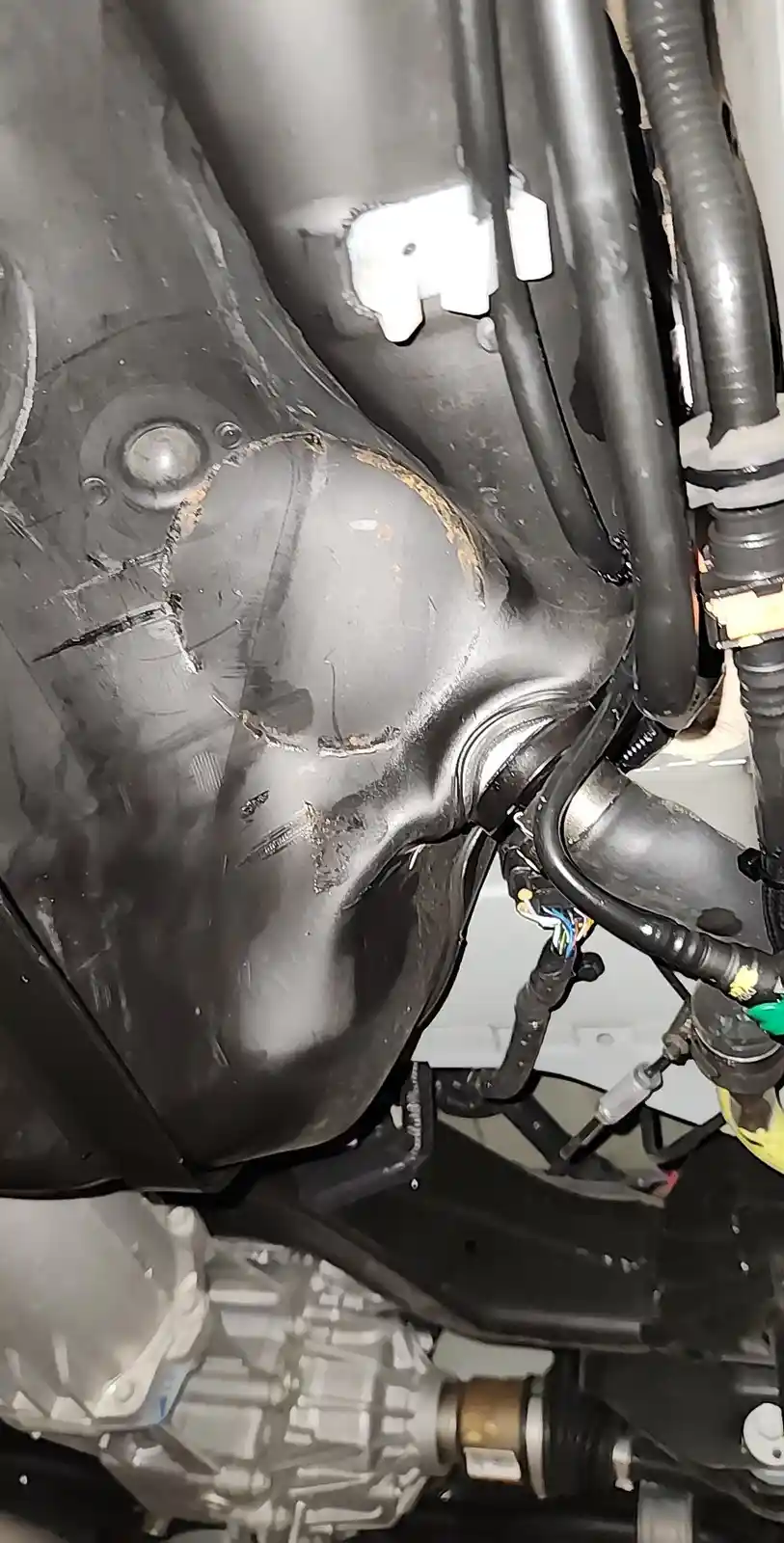 A close-up photo of a damaged, cracked black plastic car part under the vehicle, surrounded by wires and other mechanical…