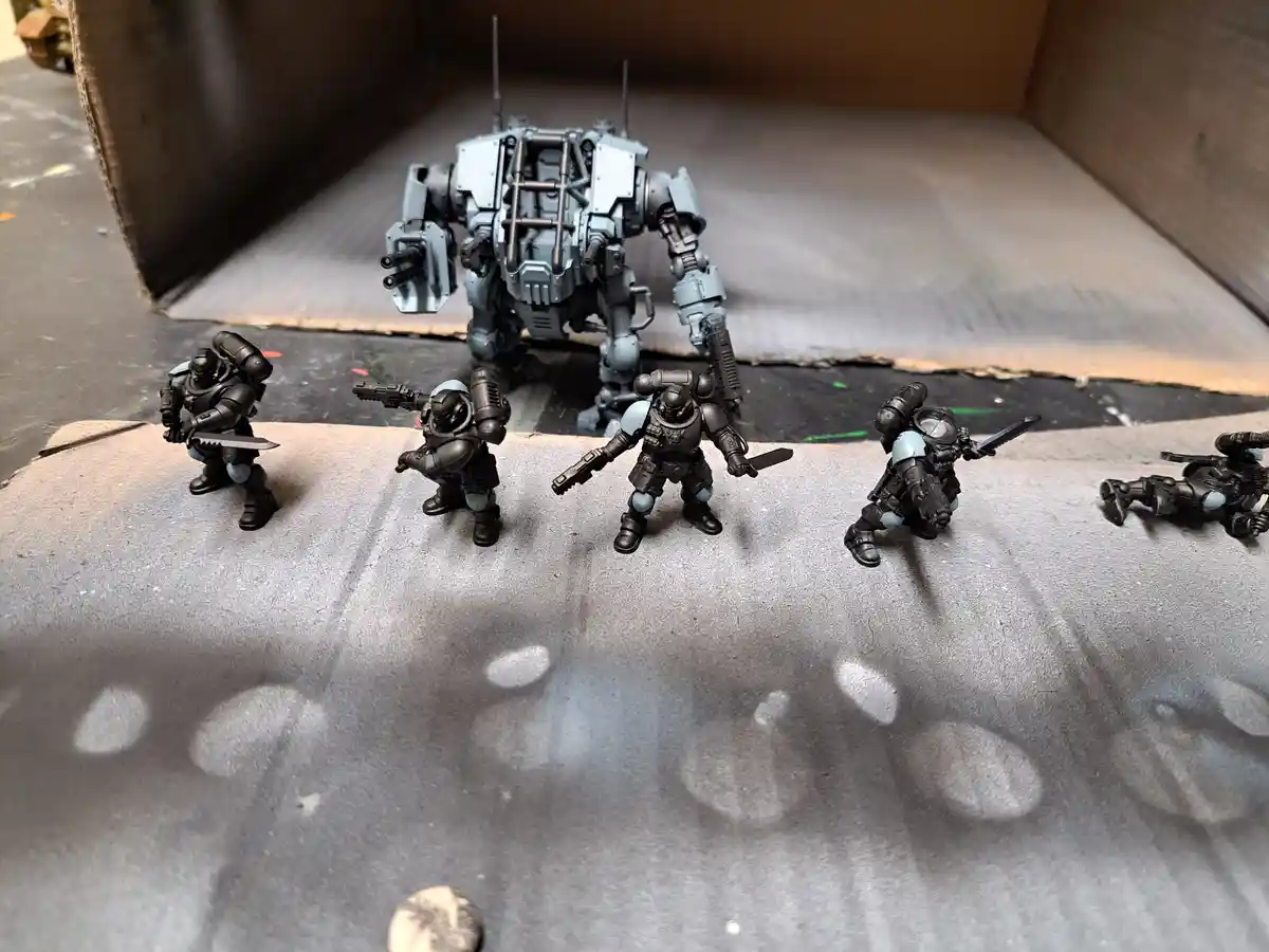 A photo shows five painted miniature soldiers in black and light blue armor standing in a line, facing a large, unpainted…