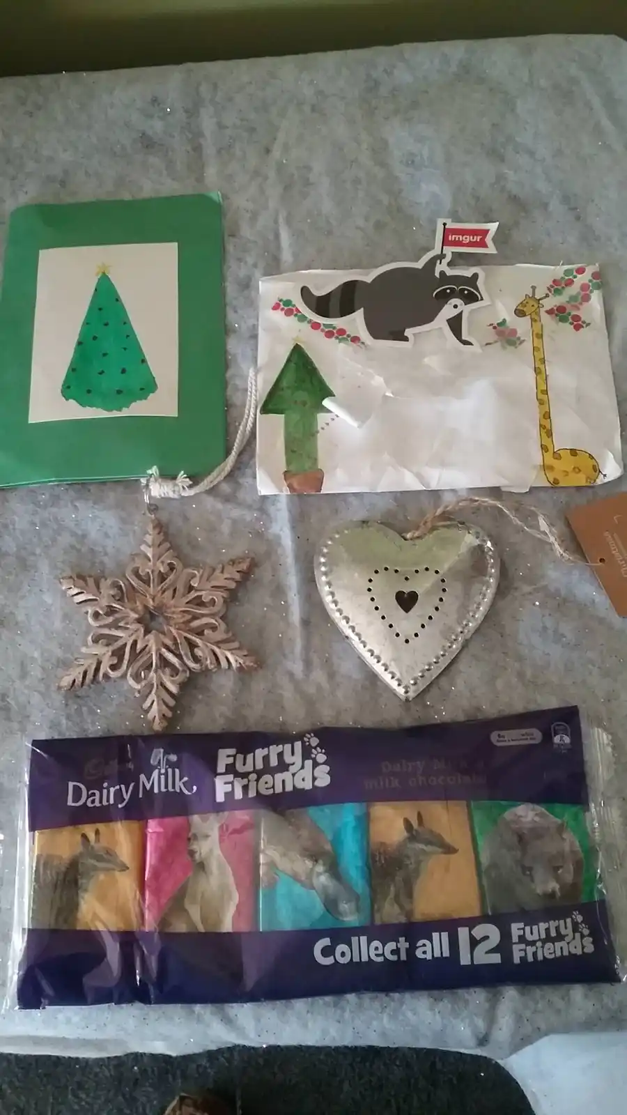 A collection of Christmas decorations including a green card with a hand-drawn tree, a paper bag with a raccoon sticker…