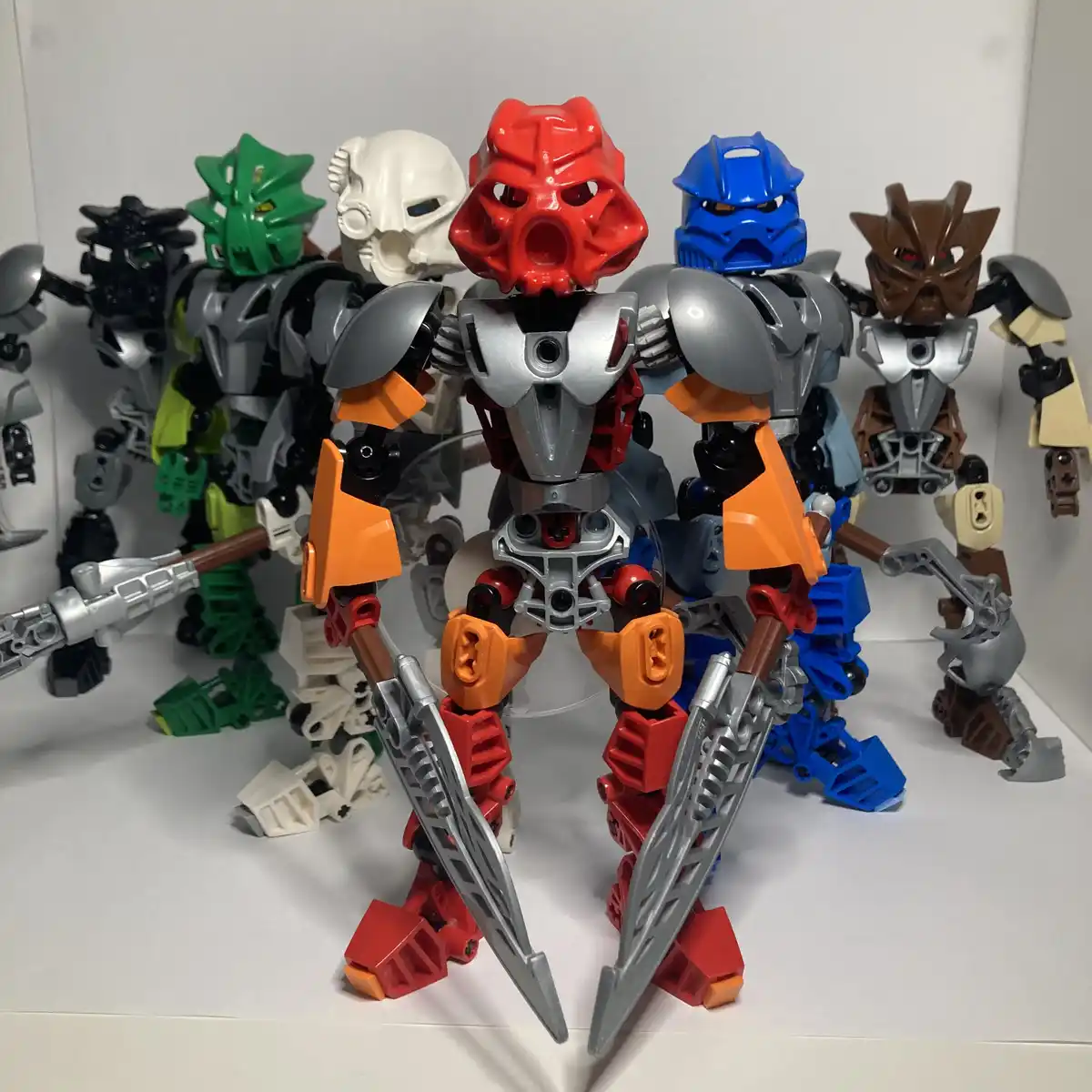 A group of Bionicle action figures, with a red one in the foreground holding two swords, stands in front of other figures in…