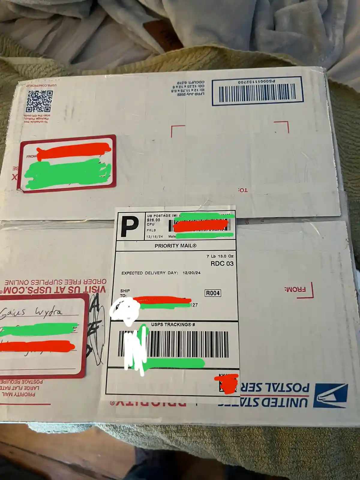 A close-up photo of a USPS Priority Mail shipping box with a label showing an expected delivery date of 12/20/24, which is…