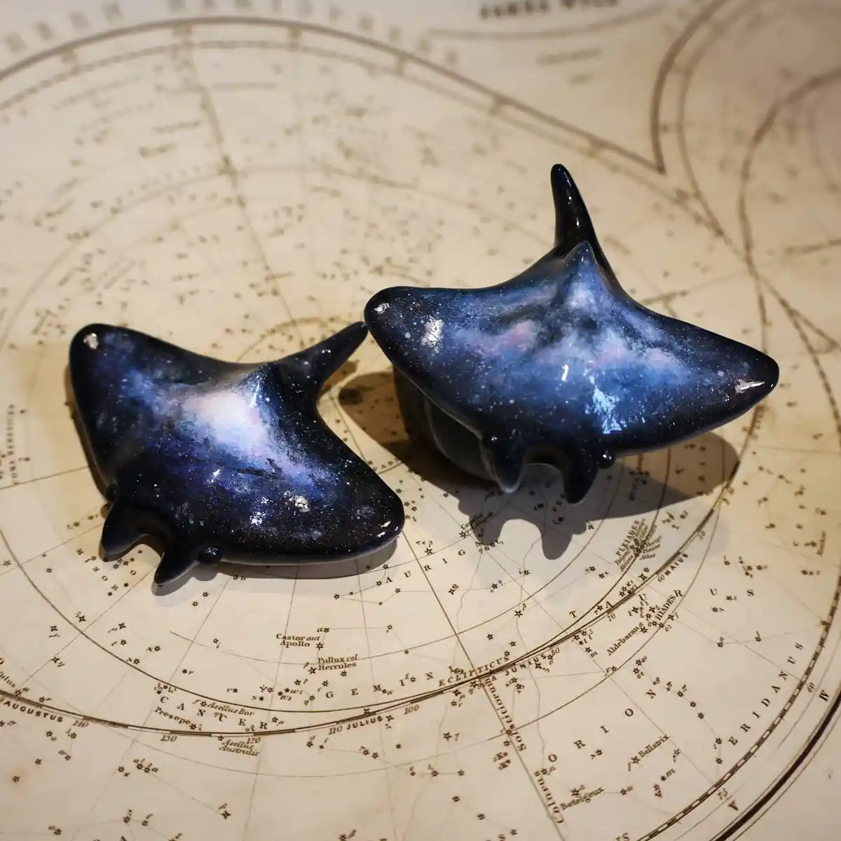 Two glossy, galaxy-patterned shark-shaped figurines sit on an antique star chart. The overlaid text reads 'i'm not a shark…