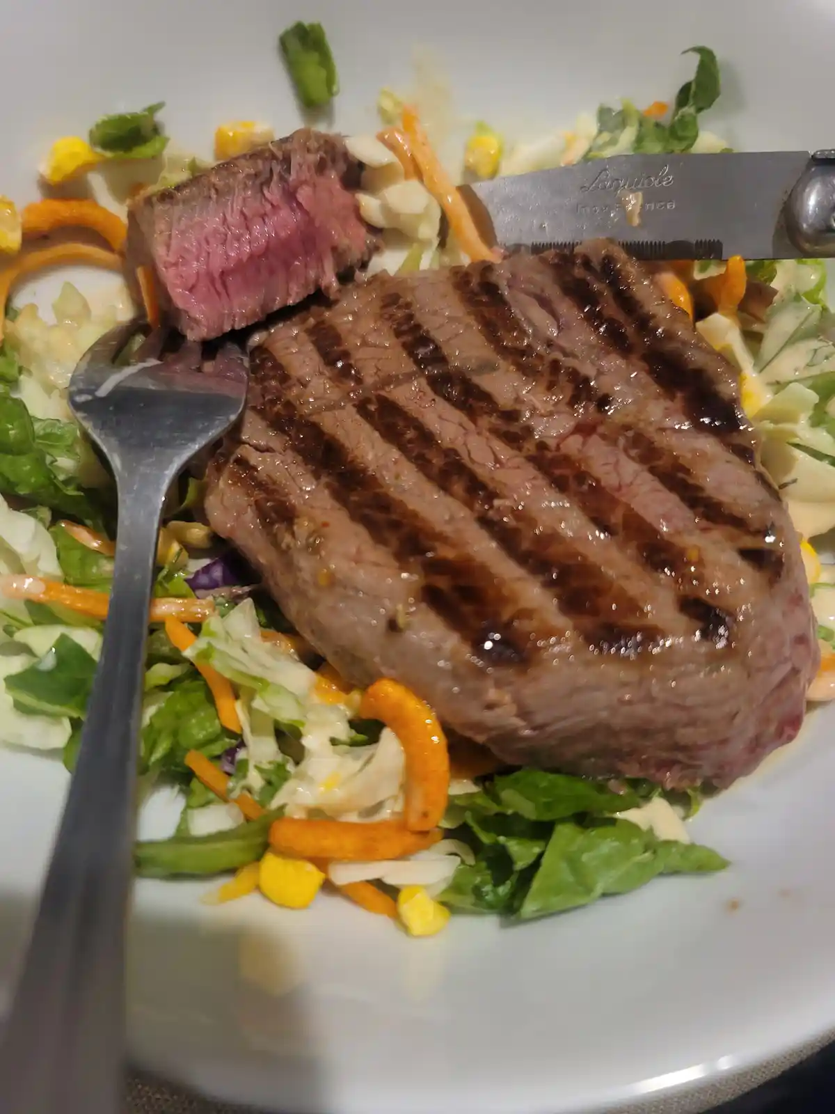 A close-up photo of a grilled steak with visible char marks, partially sliced to reveal a pink, medium-rare interior…
