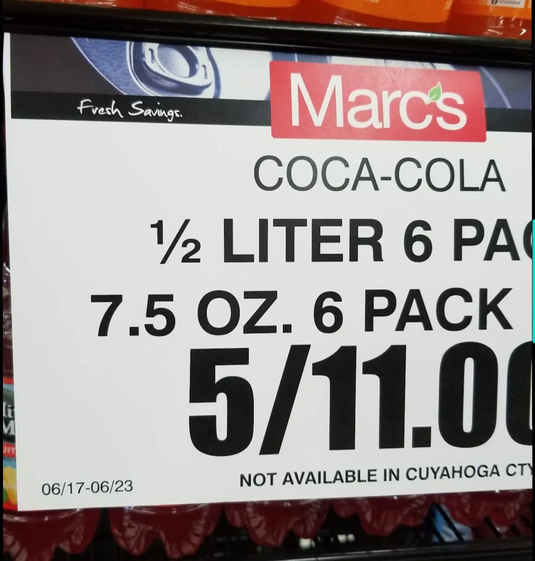 A close-up of a price tag from Marc's grocery store advertising a 1/2 liter (7.5 oz) Coca-Cola 6-pack for 5/11.00, with a…