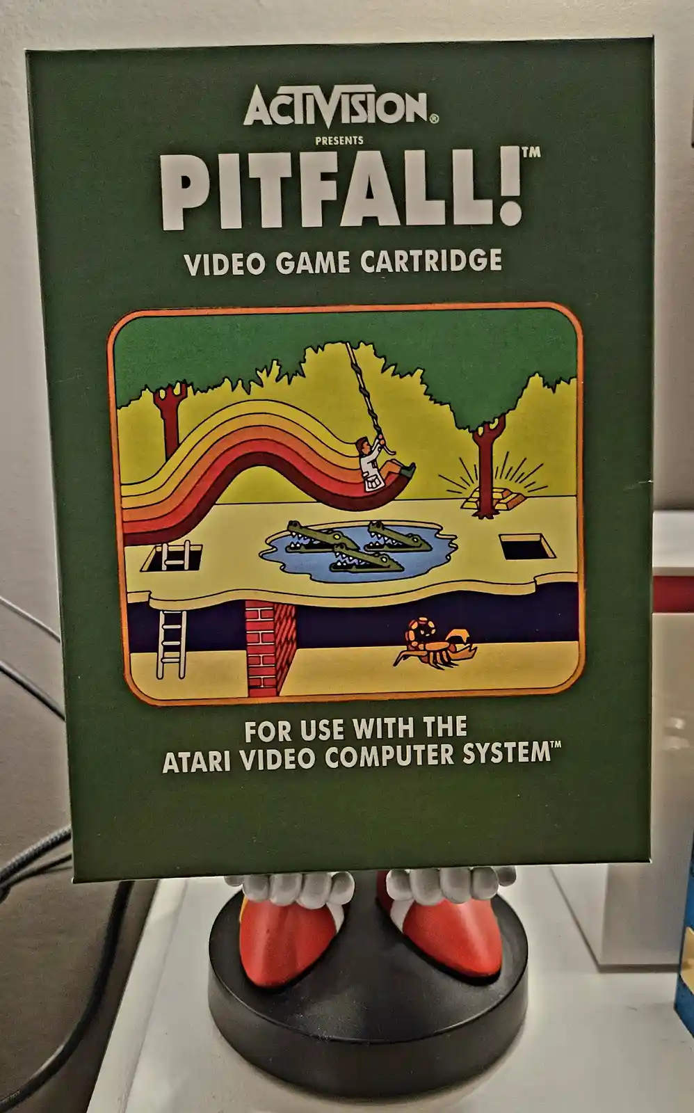 A vintage Pitfall! video game cartridge box for the Atari 2600, featuring a cartoon illustration of a character swinging on…
