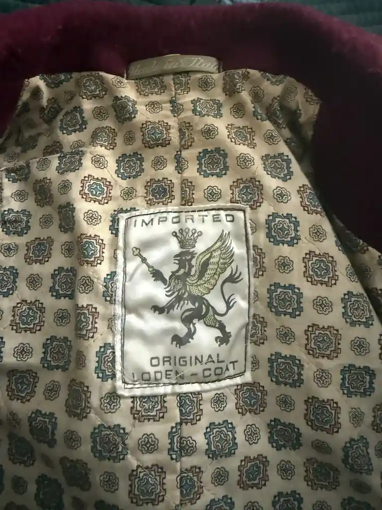 A close-up photo shows the inside lining of a coat with a repeating geometric pattern in beige, teal, and brown. A white…