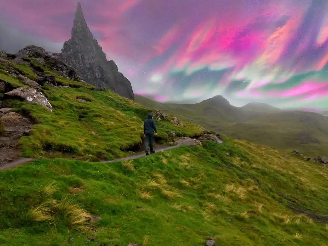 A person in a dark hoodie walks away on a grassy mountain trail, facing a dramatic, surreal sky filled with vibrant pink and…