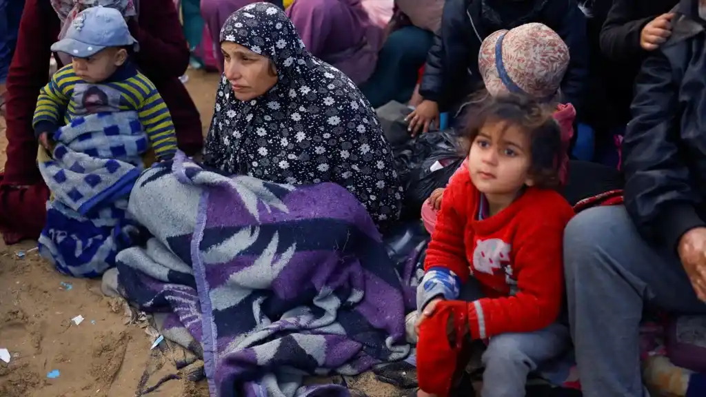 A woman and children sit on the ground wrapped in blankets, looking weary and sad. The overlaid text reads 'i'm not crying…
