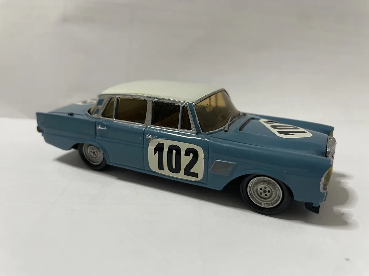 A blue and white vintage toy race car model with the number 102 prominently displayed on its side and hood, photographed…